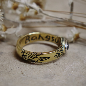 Gold ring with engraved design on a textured surface with dried flowers in the background