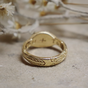 Gold ring with engraved design on a textured surface with dried flowers in the background