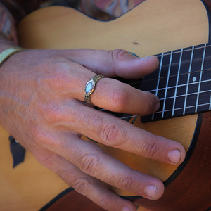 Close-up of a person's hand playing an acoustic guitar with a gold ring on the finger.