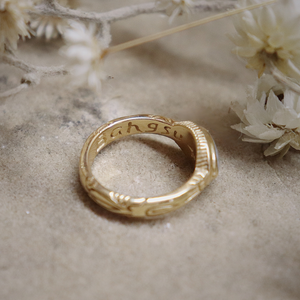 Gold ring with engraved text on a textured surface with dried flowers