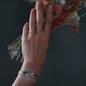 Hand holding dried flowers with a gold ring and bracelet on a dark background