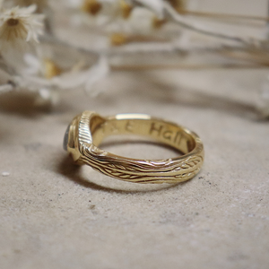 Gold ring with engraved text on a textured surface with dried flowers in the background