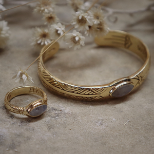 Gold bracelet and ring with engraved details on a textured surface with dried flowers.