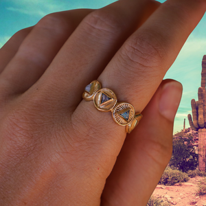 Gold ring with triangular designs on a hand against a desert background